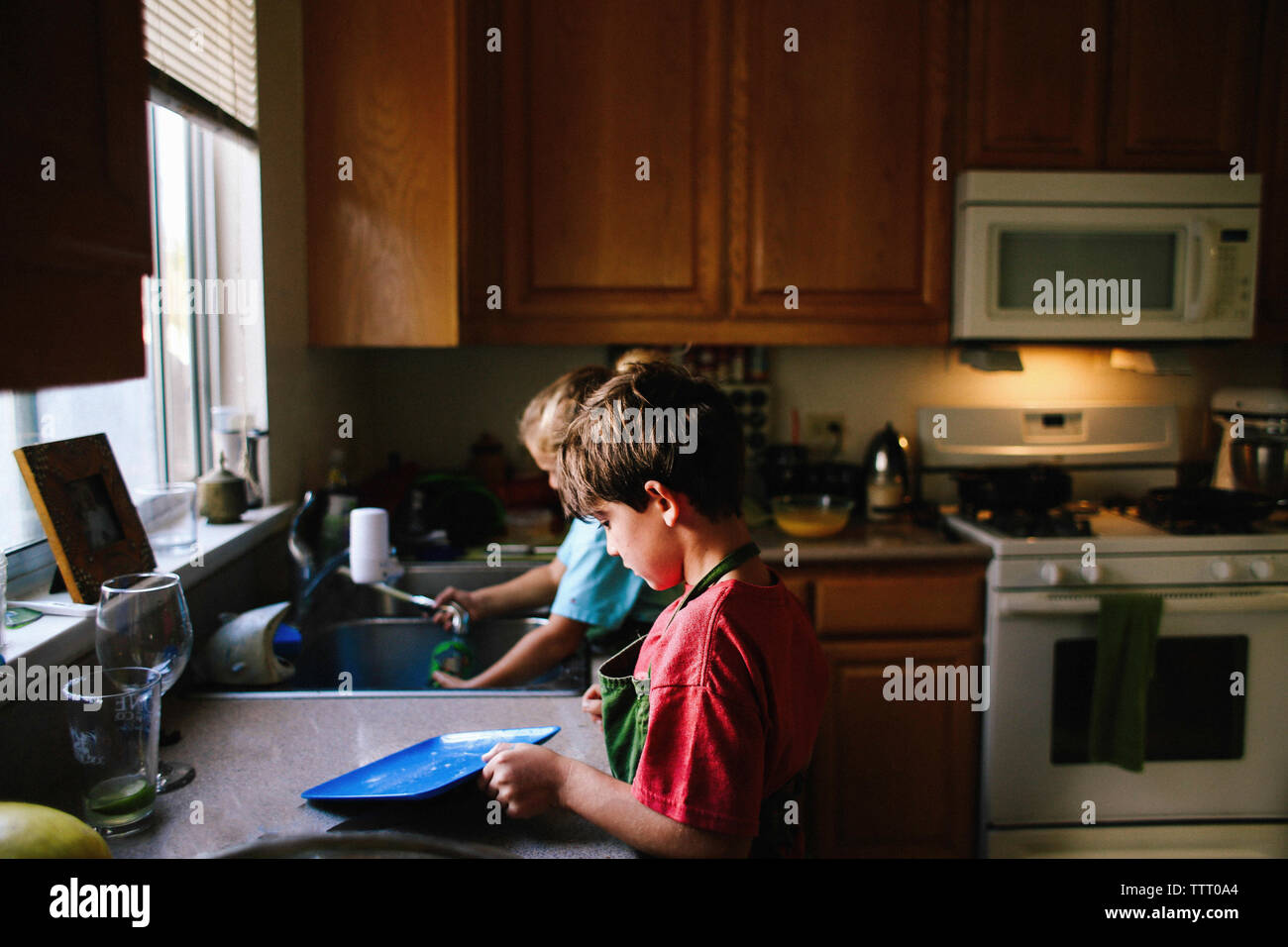 Siblings cleaning utensils in kitchen Stock Photo