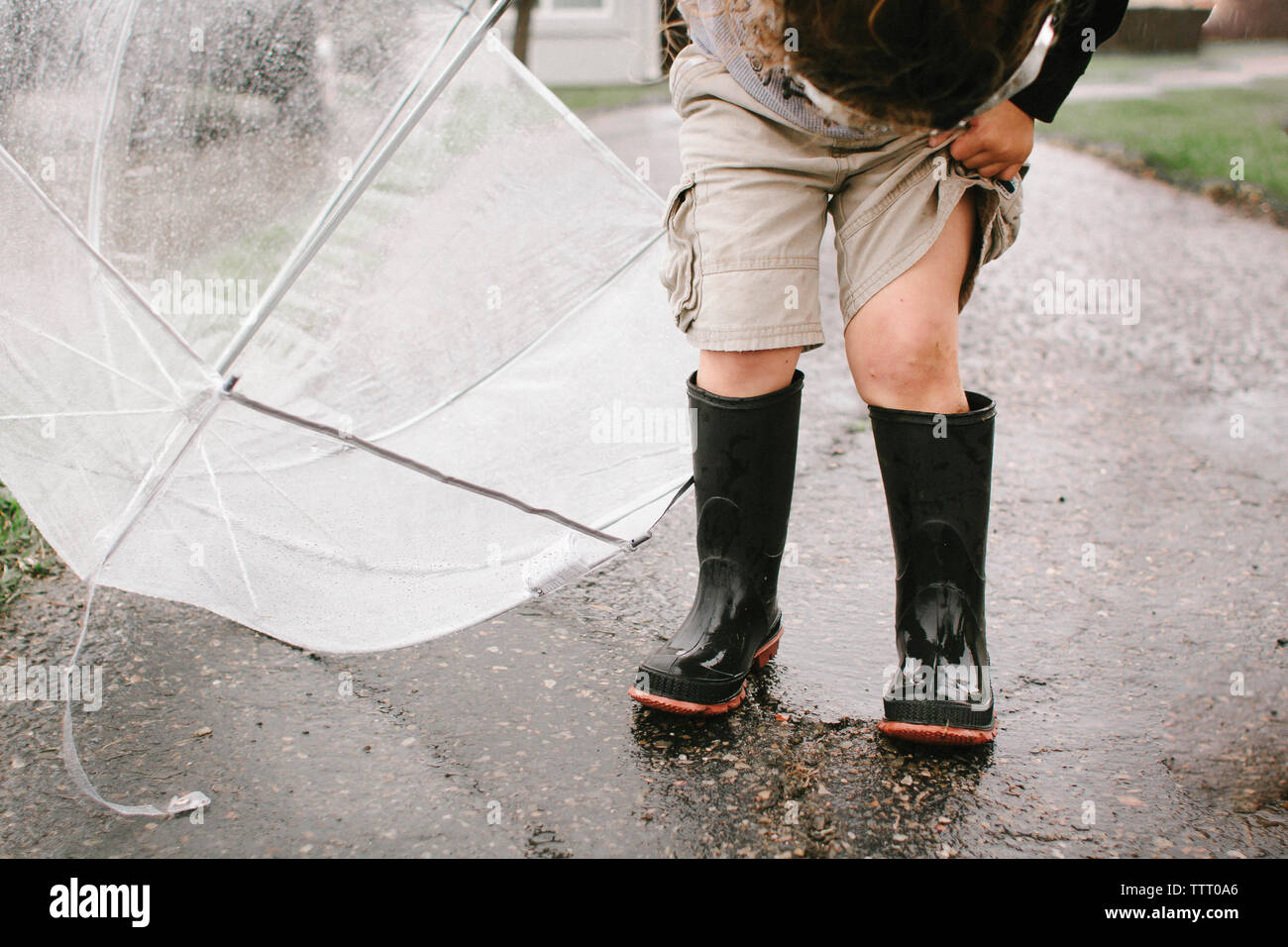 Girl in rubber boots holding umbrella while standing on wet road Stock Photo