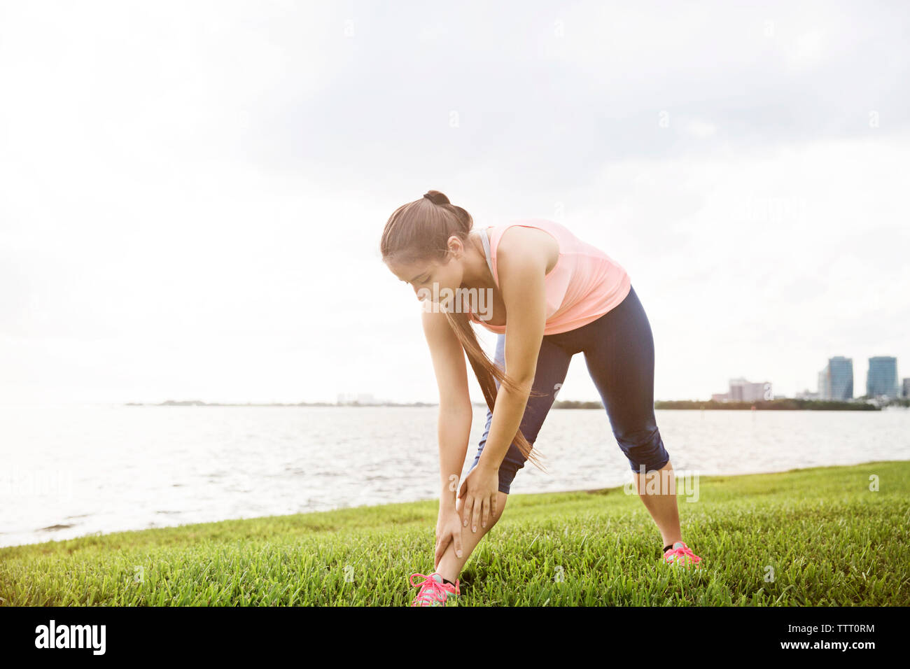 Young woman exercising on grassy field against sea and sky Stock Photo