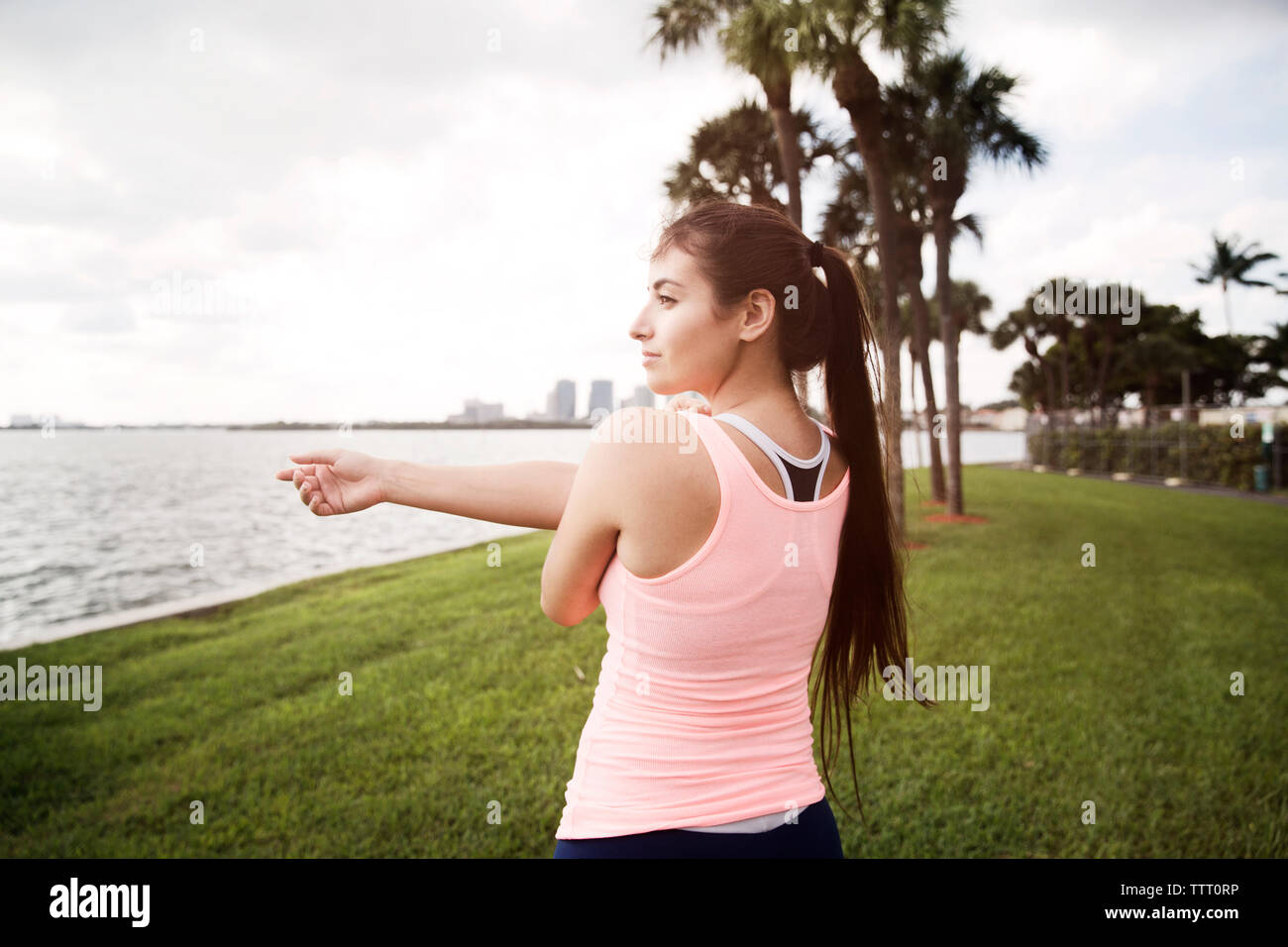 Female athlete stretching arm at grassy field against sky Stock Photo