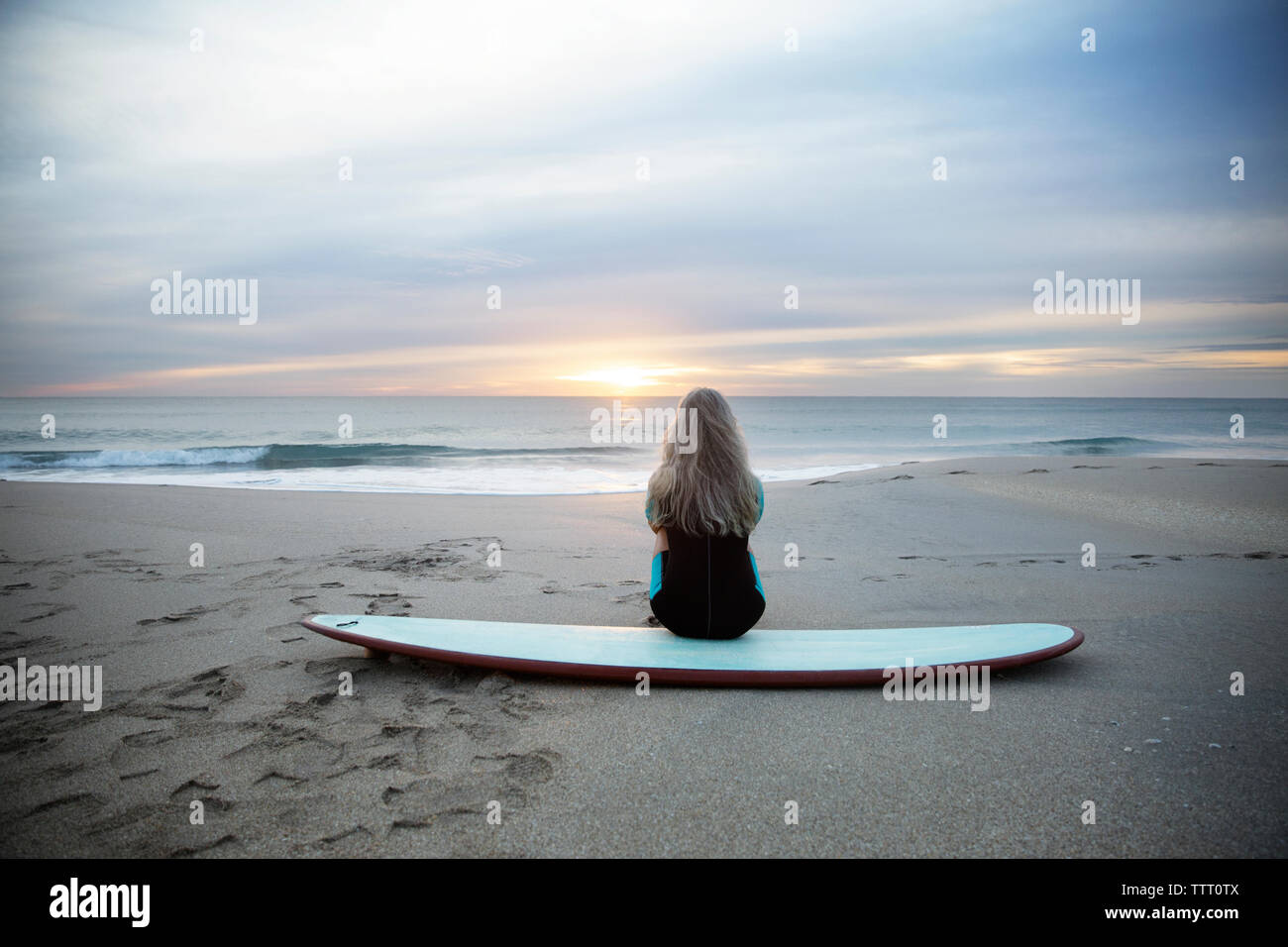 Female surfer sitting on surfboard at sunset hi-res stock photography ...