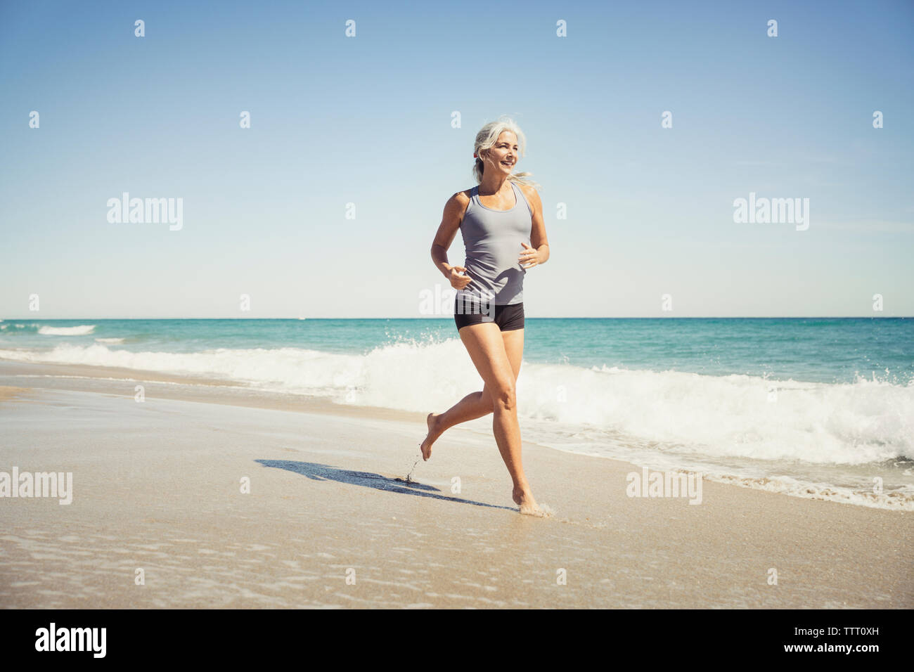 Full length of mature woman jogging on sea shore at Delray beach Stock Photo