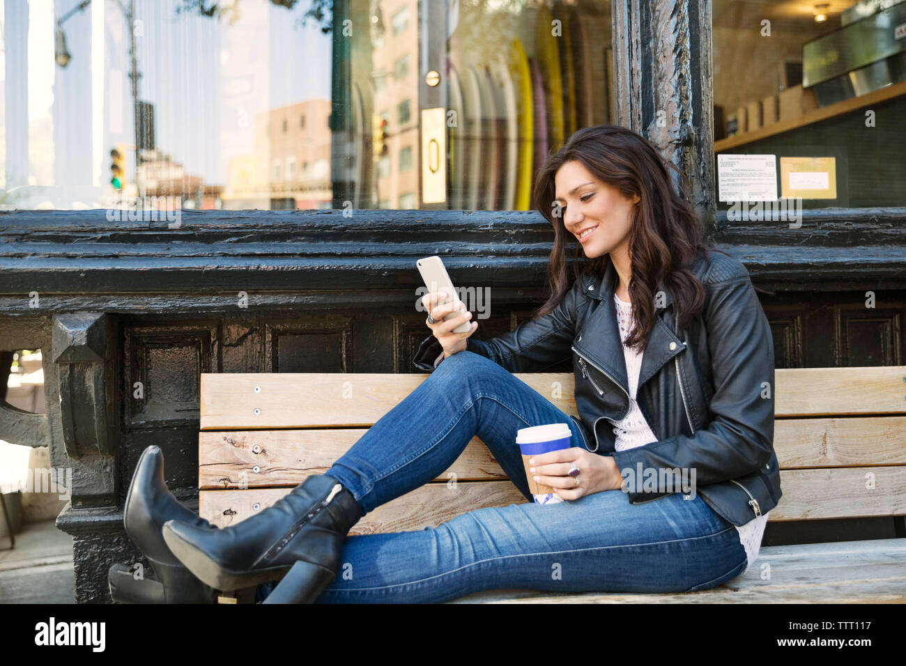 Happy woman using smart phone while sitting on bench at sidewalk cafe Stock Photo