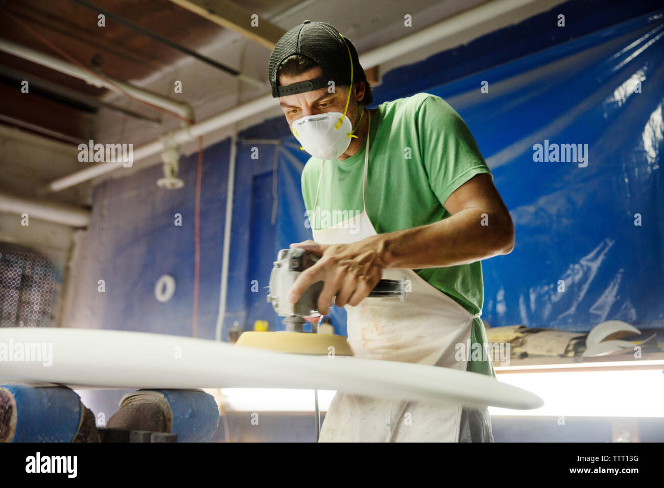 worker using sander machine on surfboard in workshop Stock Photo