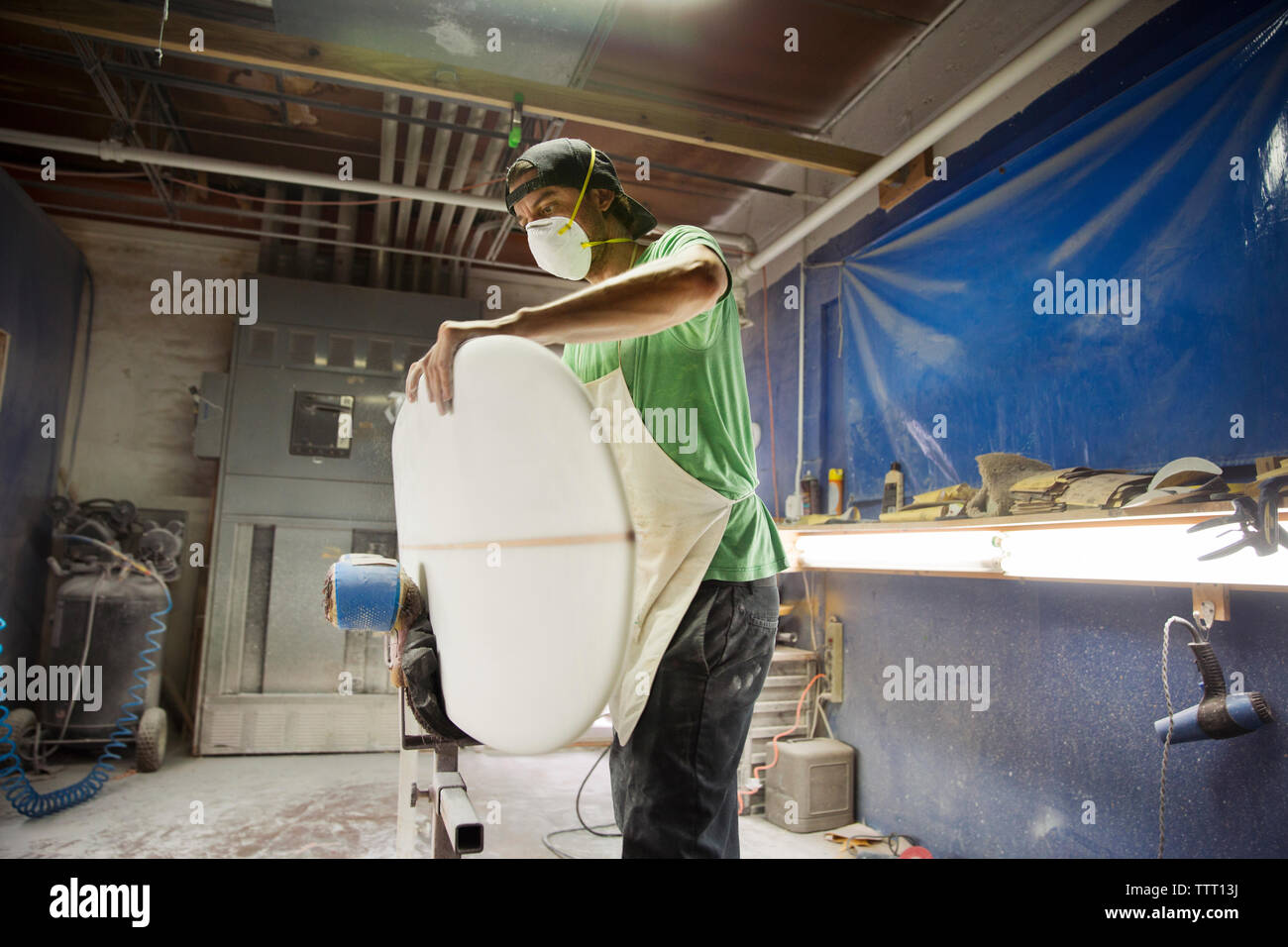 worker holding surfboard while standing in workshop Stock Photo