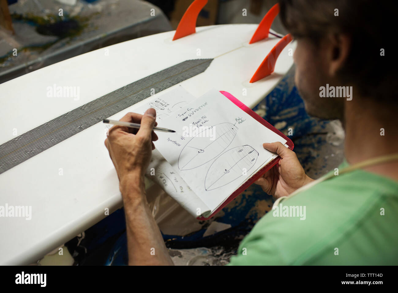 worker writing in book while analyzing surfboard in workshop Stock Photo