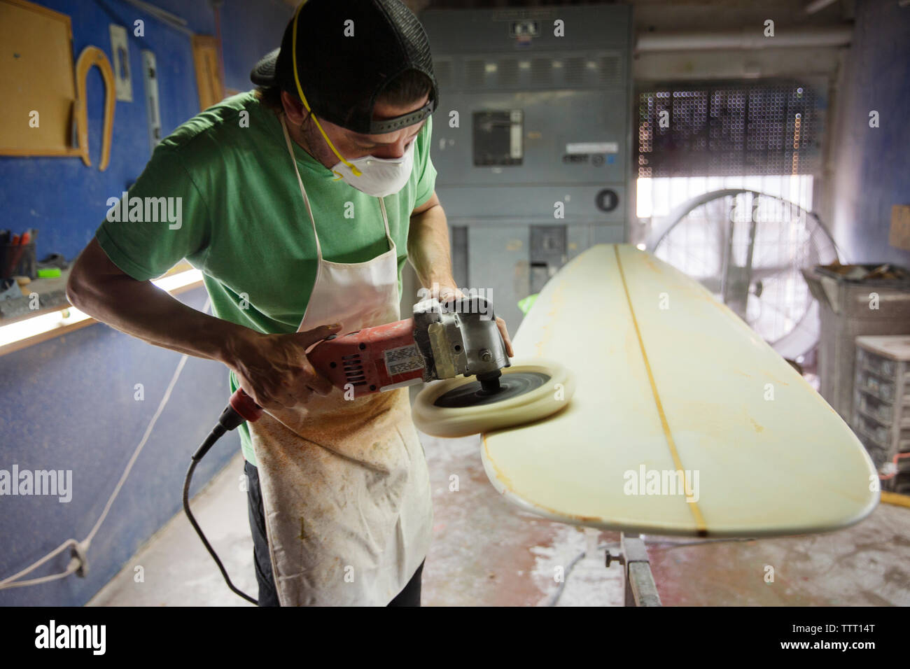 Male worker using sander on surfboard in workshop Stock Photo