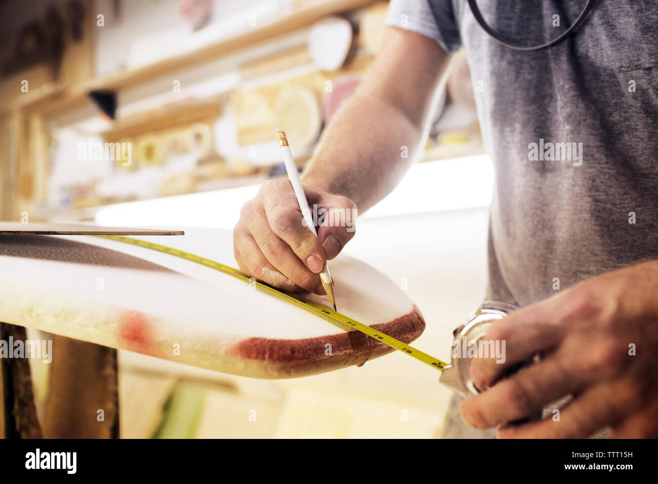 Midsection of man measuring surfboard at workshop Stock Photo