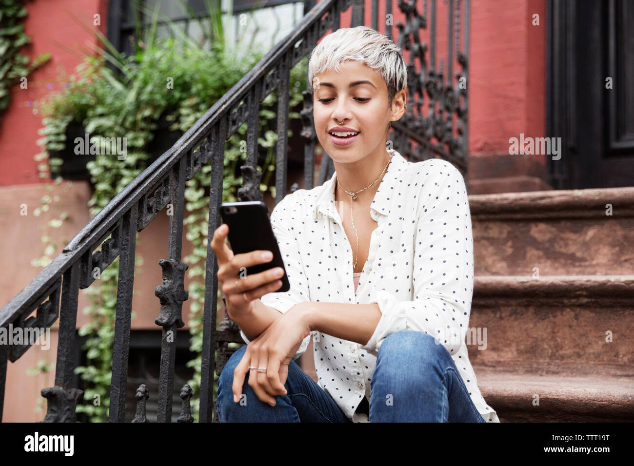 Happy woman using mobile phone while sitting on steps Stock Photo