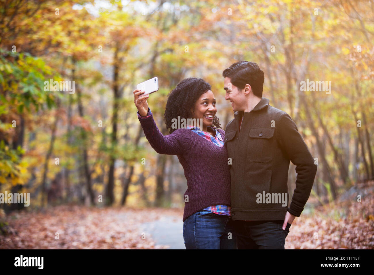 Happy couple looking at each other while taking selfie in forest Stock Photo