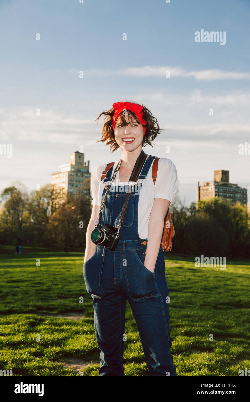 Happy woman with hands in pockets standing on grassy field at park ...