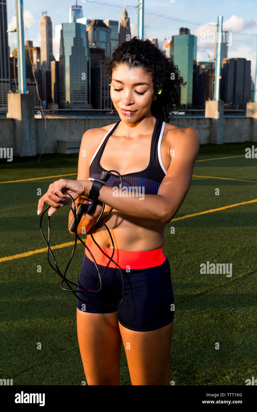 Female athlete using smart watch while standing on grassy field during sunset Stock Photo