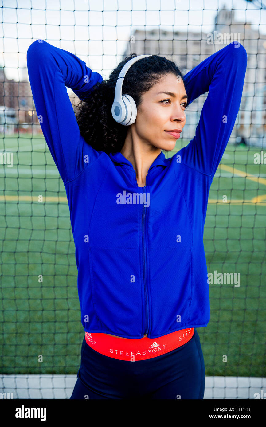 Confident female athlete with arms raised listening music while standing by net Stock Photo