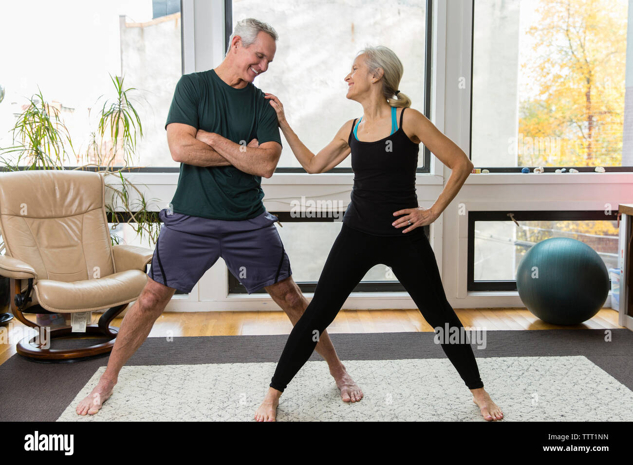 Smiling woman talking with man while exercising against windows at home Stock Photo