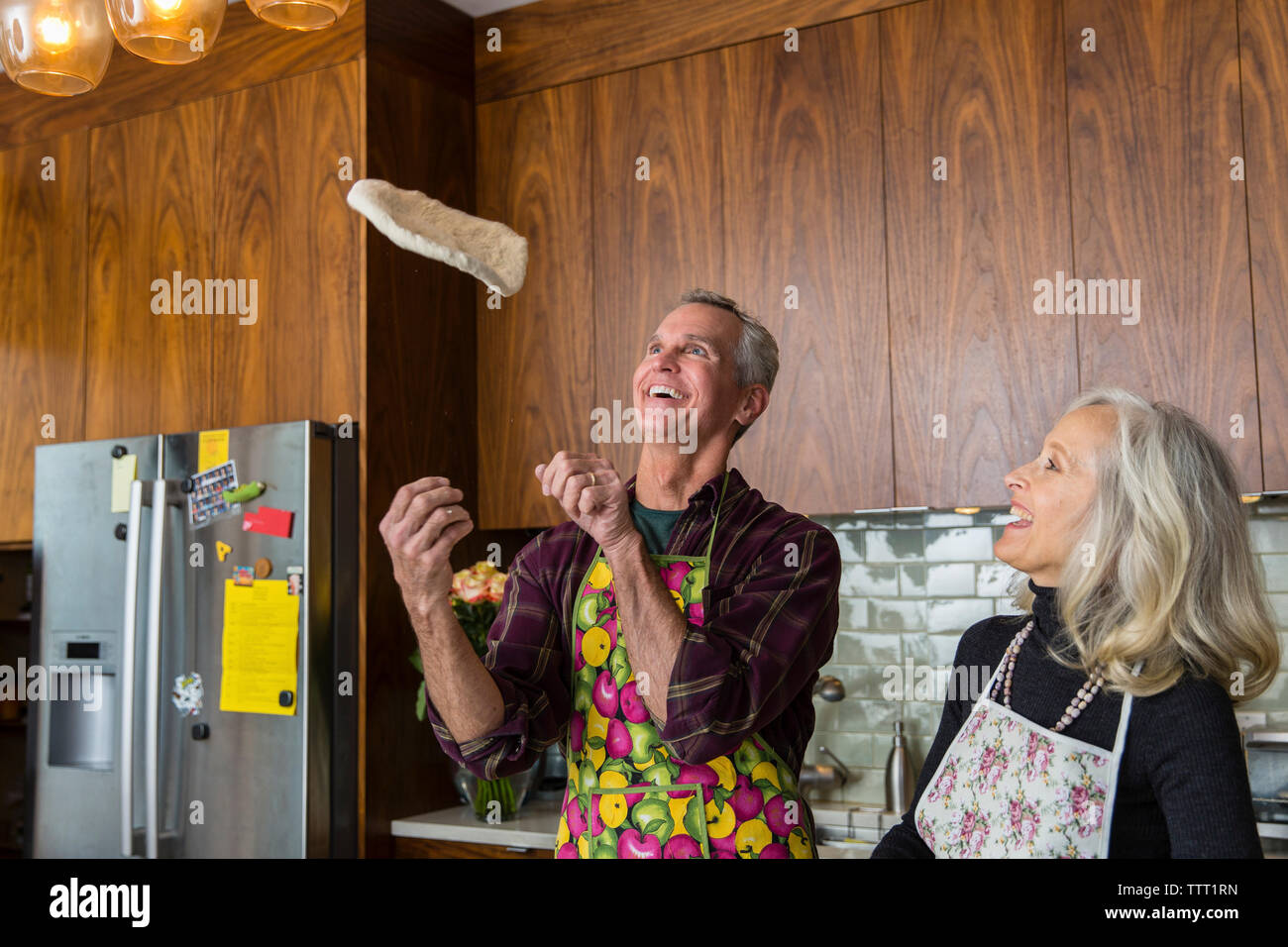 Cheerful man tossing pizza dough while preparing food by woman in kitchen at home Stock Photo