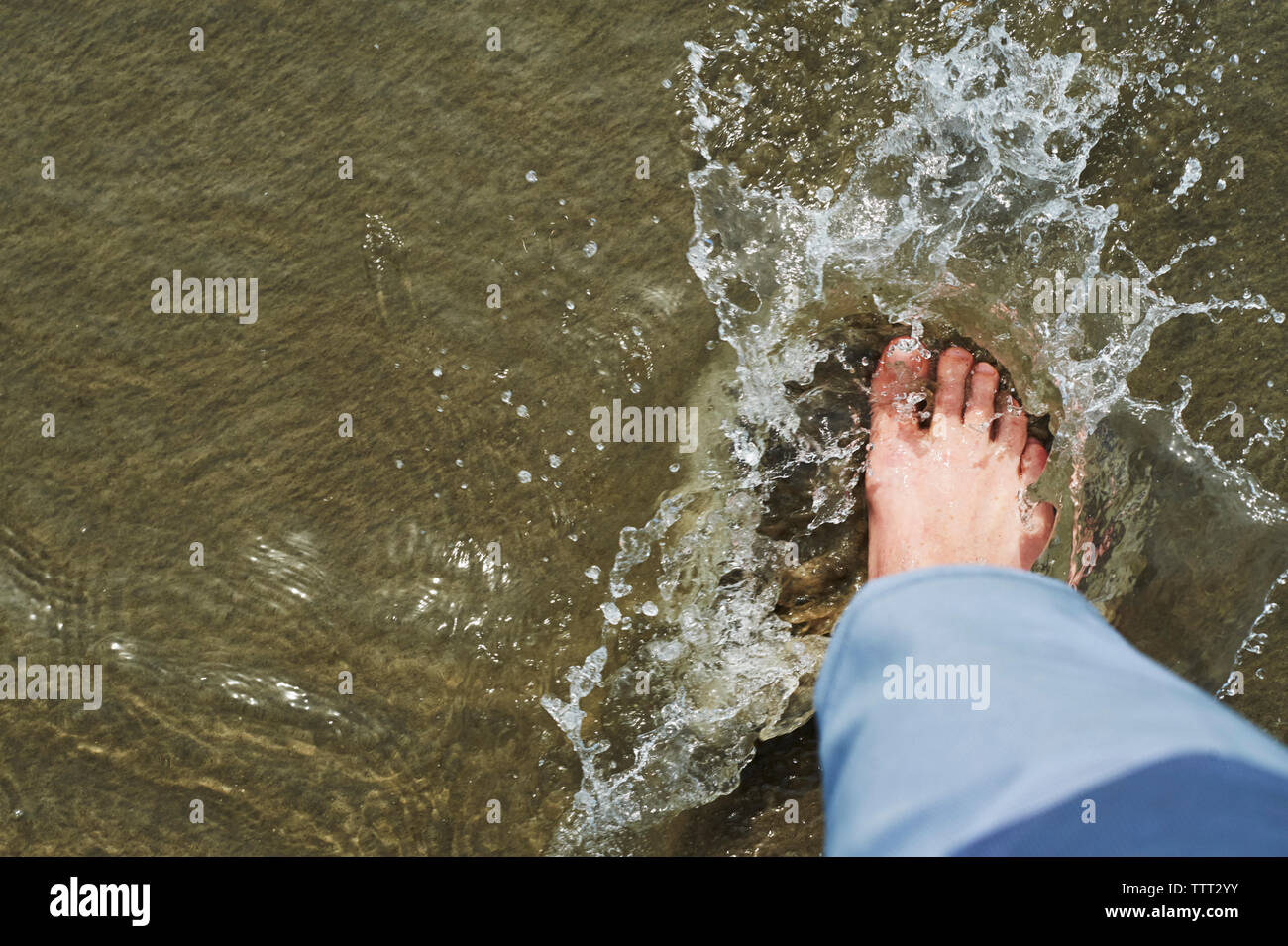 Low section of man stamping foot in water on shore Stock Photo