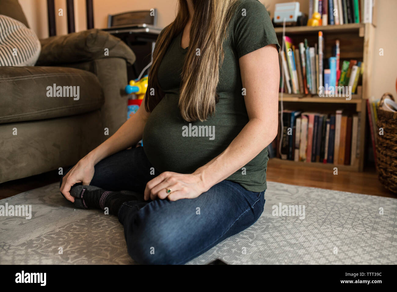 Low section of pregnant woman sitting on carpet at home Stock Photo