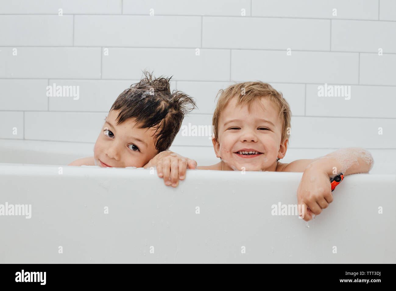 Siblings taking bubble bath in white tub with smiles Stock Photo