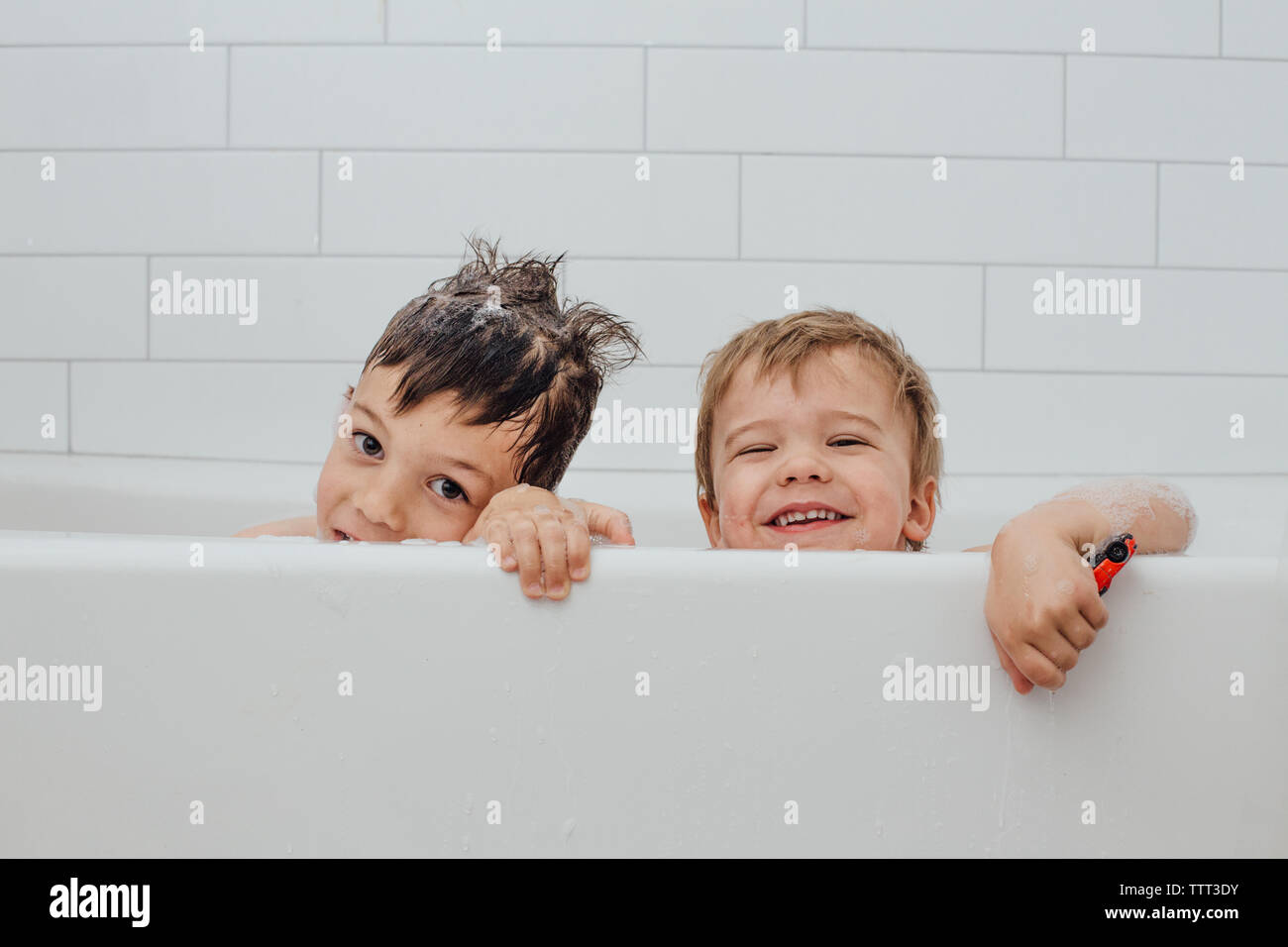 Boys sticking head out of bubble bath with big smiles Stock Photo