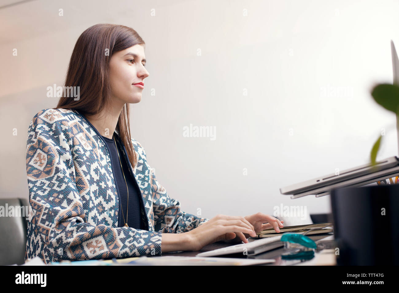 Serious businesswoman typing on computer keyboard by wall at office Stock Photo