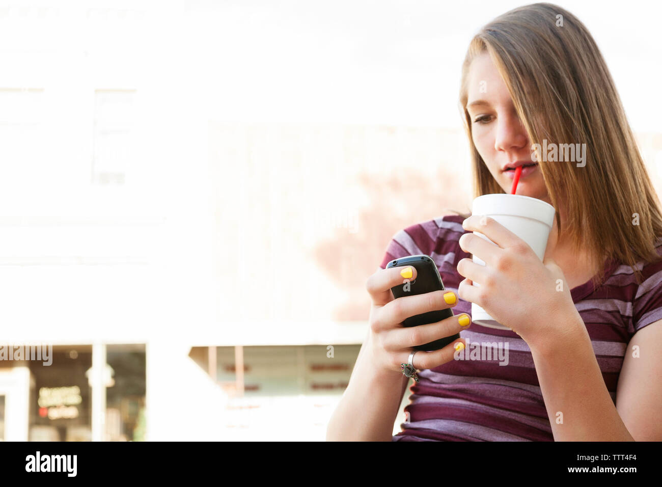Teenage girl using mobile phone while sipping drink Stock Photo