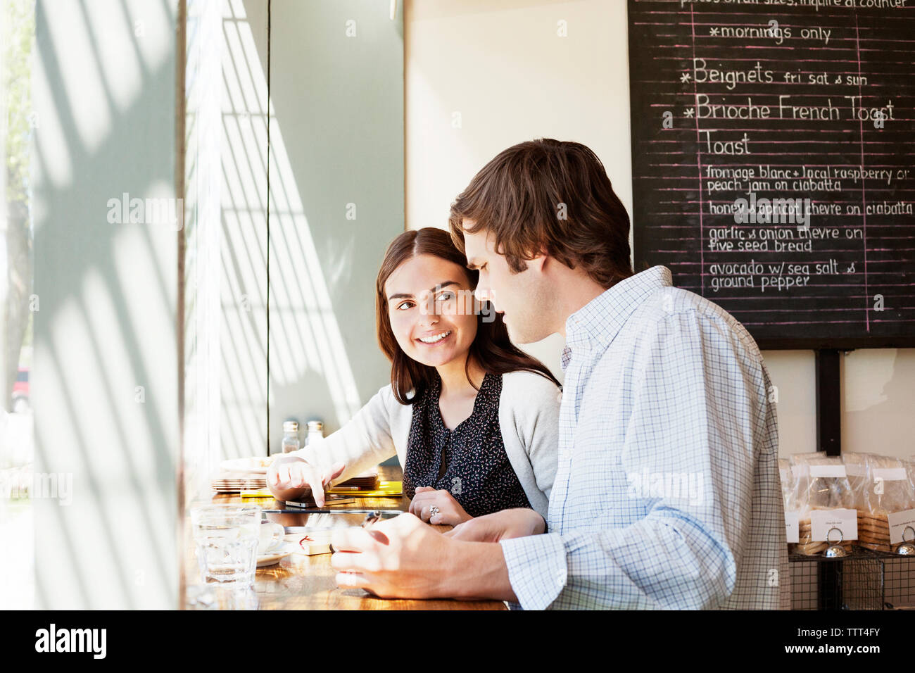 Woman pointing at tablet computer while sitting with friend at cafe Stock Photo