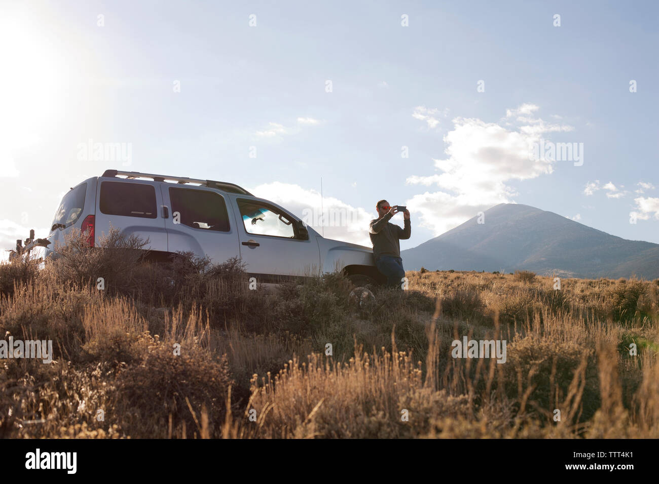 Man photographing while standing by car on field Stock Photo
