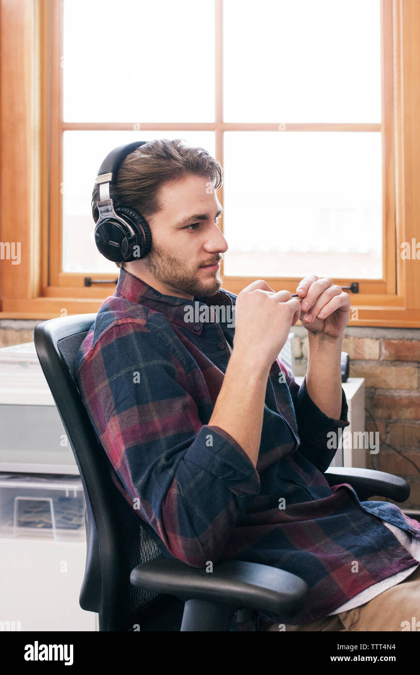 Side view of businessman wearing headphones sitting on office chair Stock Photo