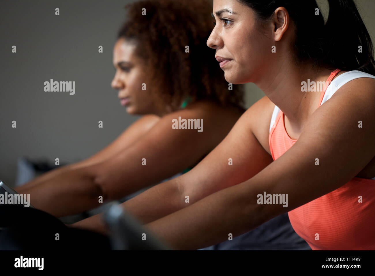 Plus size female friends exercising on exercise bikes in gym Stock Photo