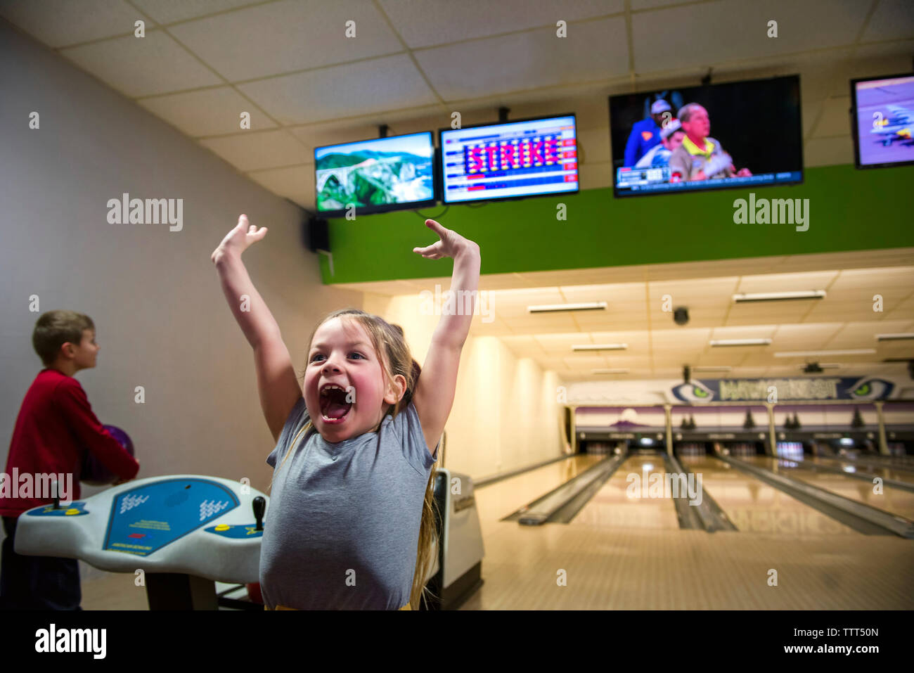 Excited sister screaming while brother holding ball at bowling alley Stock Photo