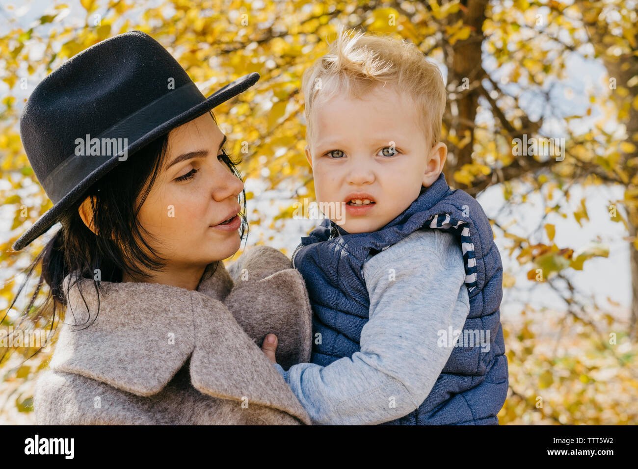 Mother carrying cute son while standing against trees in park during autumn Stock Photo