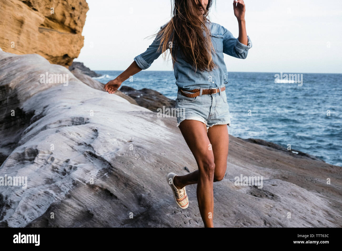 Close up of a woman running on rock formations with sea in background Stock Photo