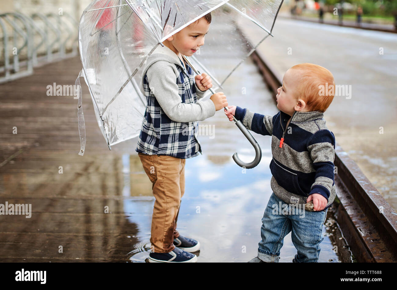 Baby boy with brother holding umbrella while standing on wet street Stock Photo