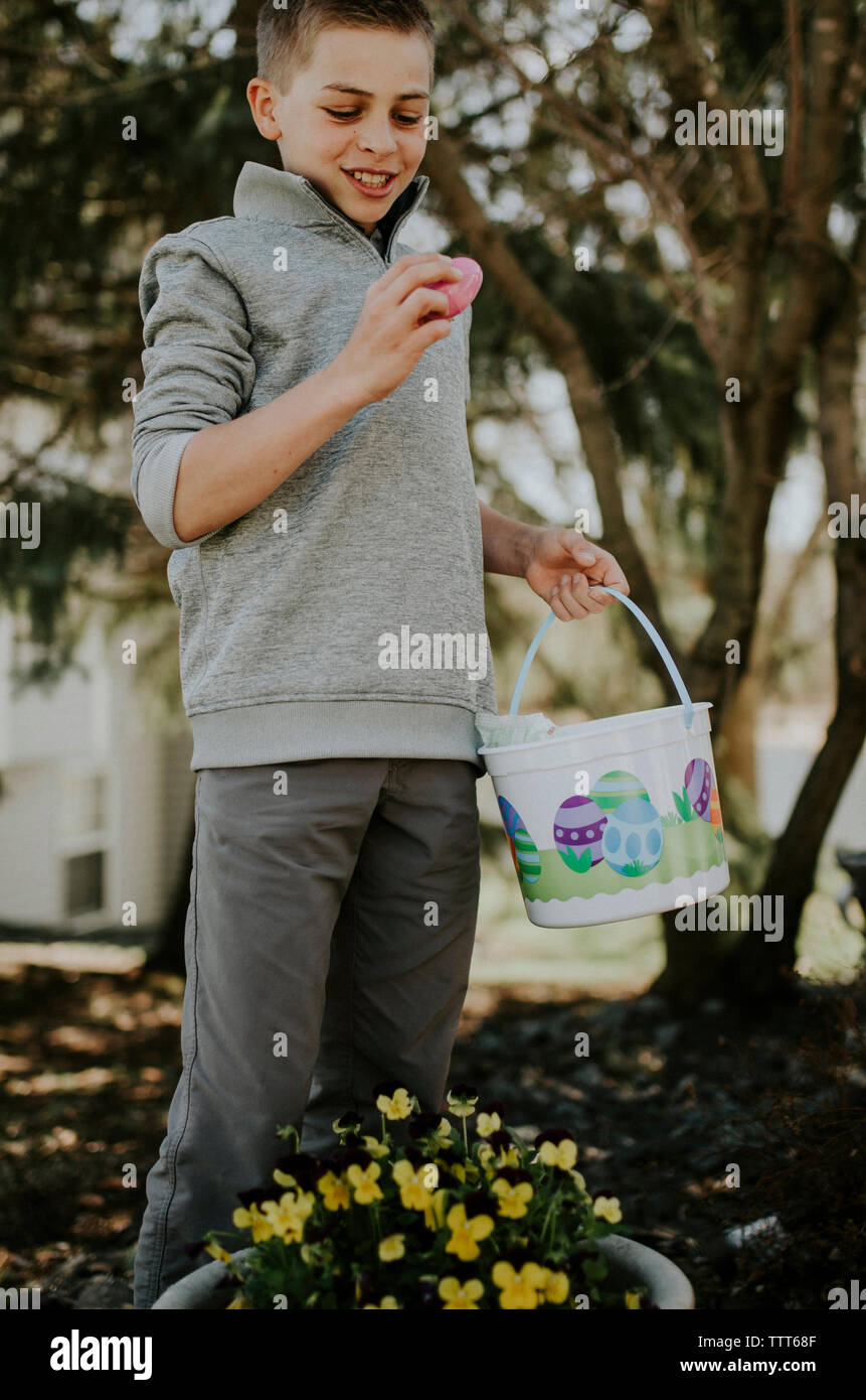 Boy looking at easter Egg while holding bucket at yard Stock Photo