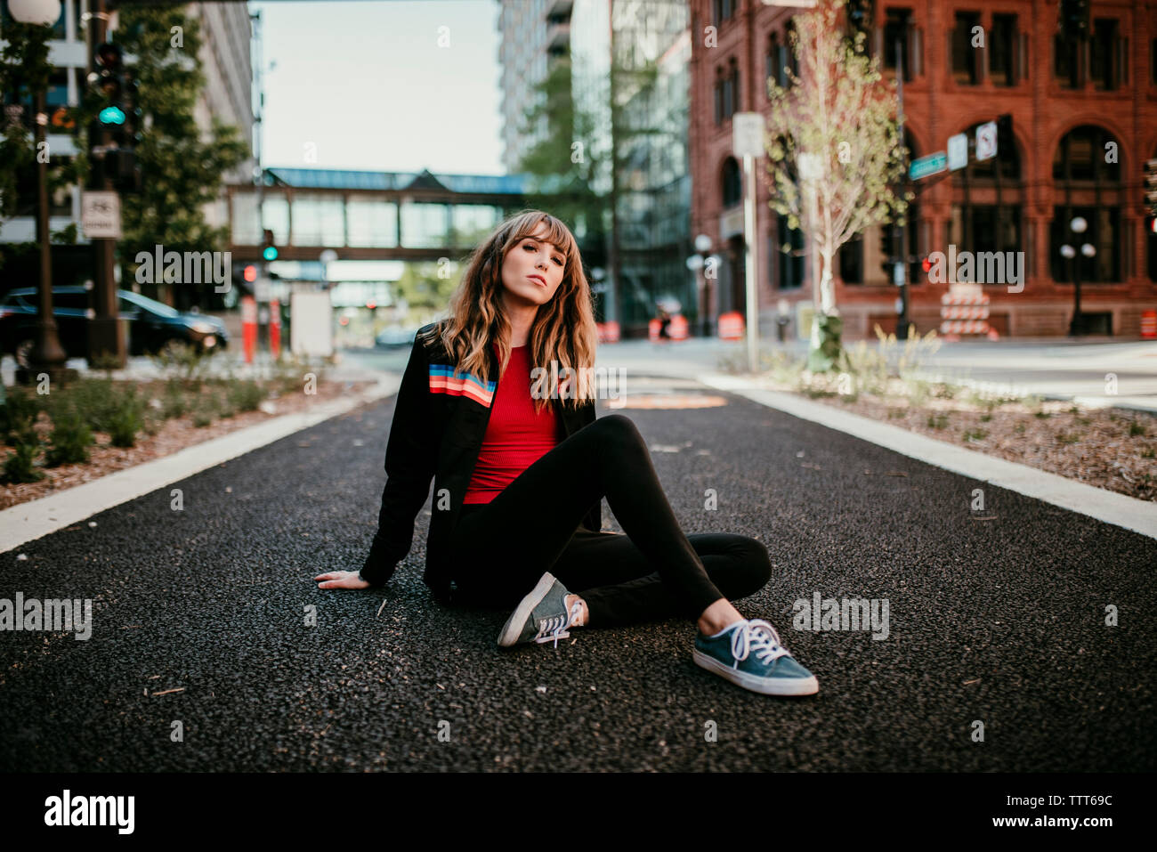 Portrait of young woman sitting on city street Stock Photo - Alamy