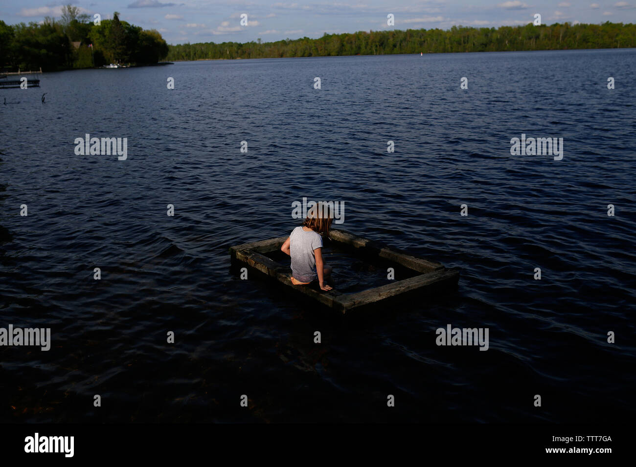Rear view of girl kneeling on wood in lake Stock Photo