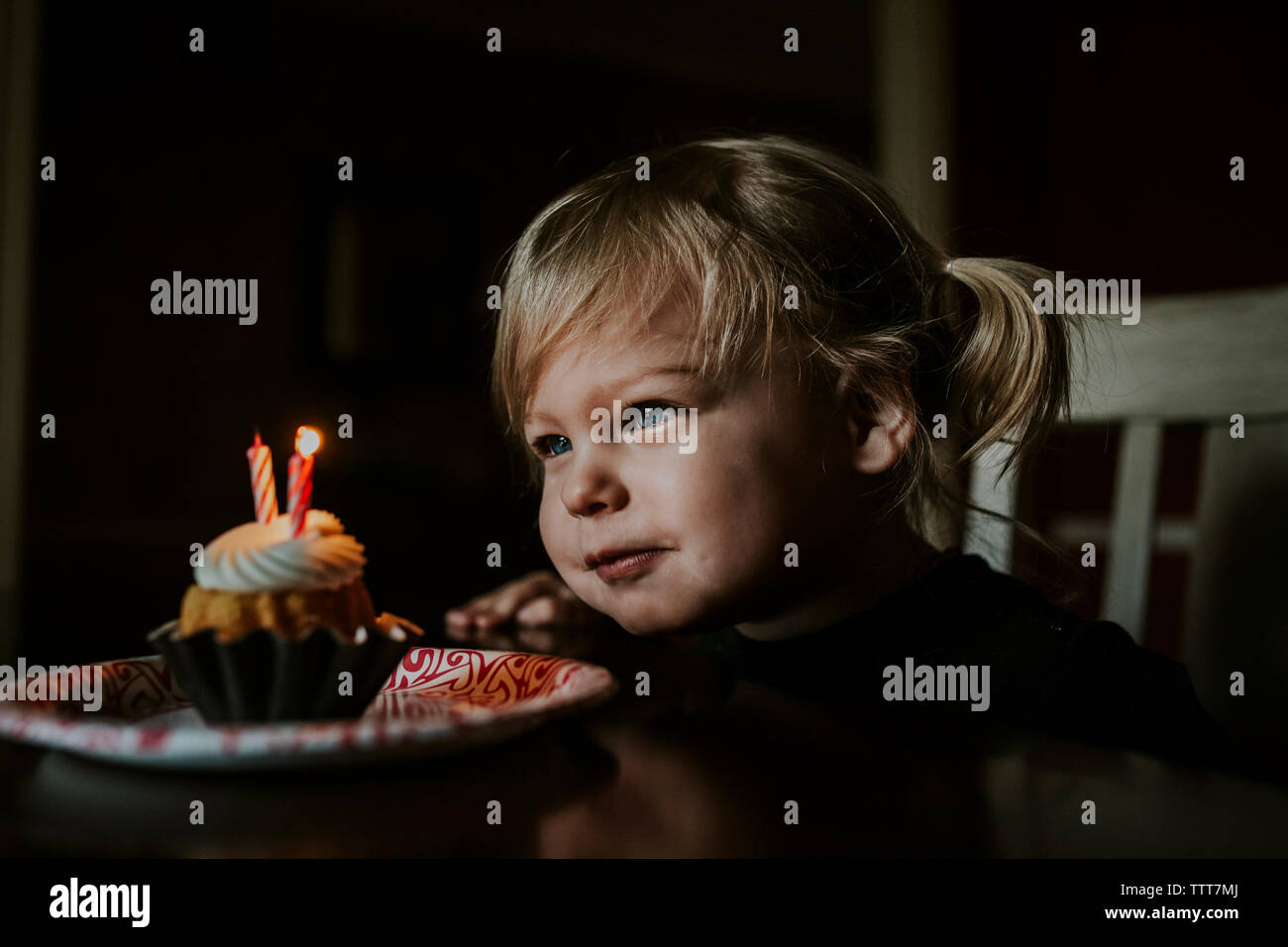 Cute girl looking at her birthday cake on table Stock Photo