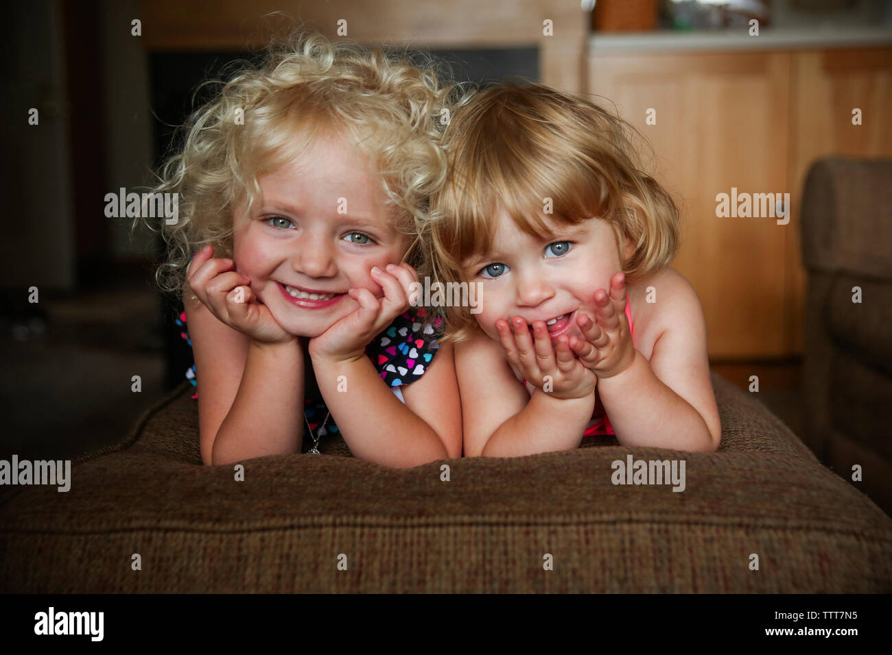 Portrait of cute sisters lying on sofa at home Stock Photo