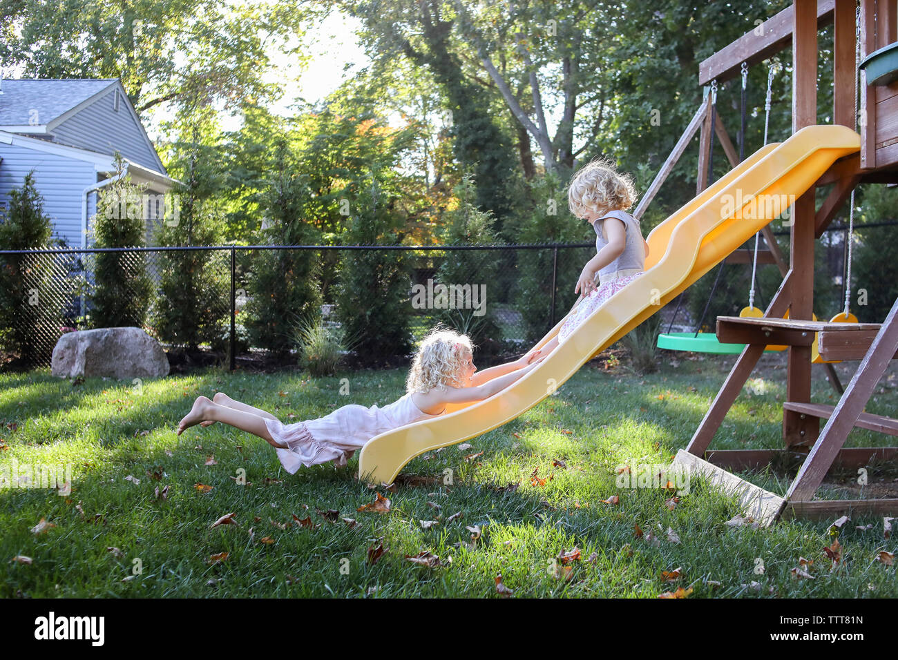Sisters playing on slide at playground Stock Photo