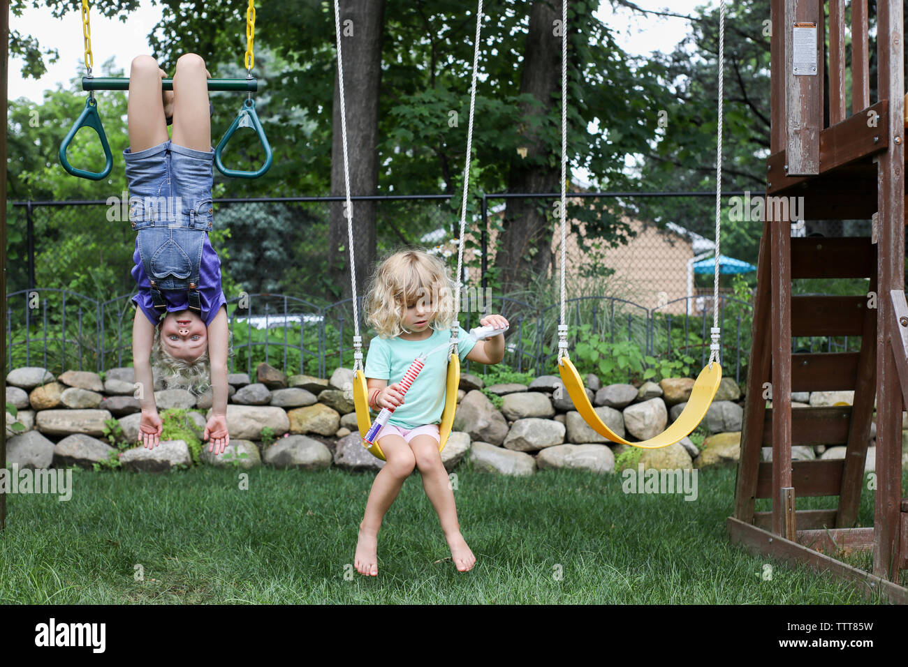 Girl hanging upside down while sister swinging at playground Stock Photo