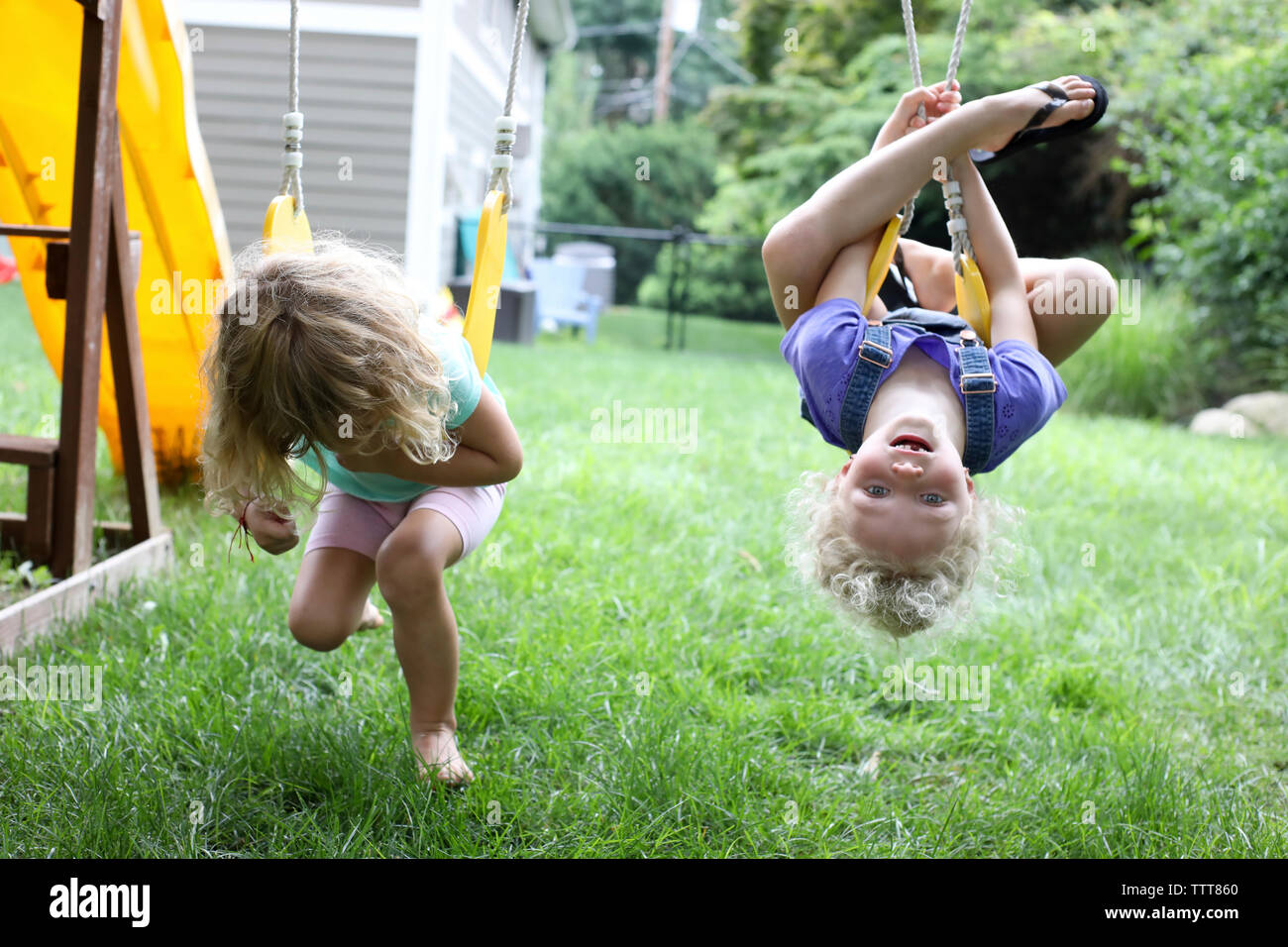 Playful sisters swinging over grassy field at playground Stock Photo