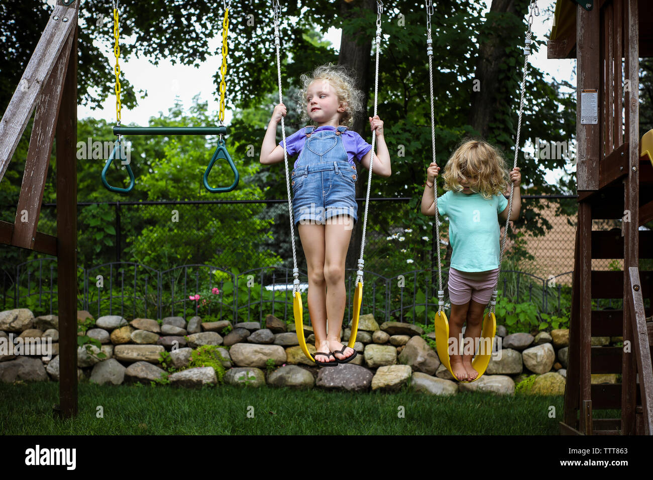 Full length of sisters playing on swings at playground Stock Photo
