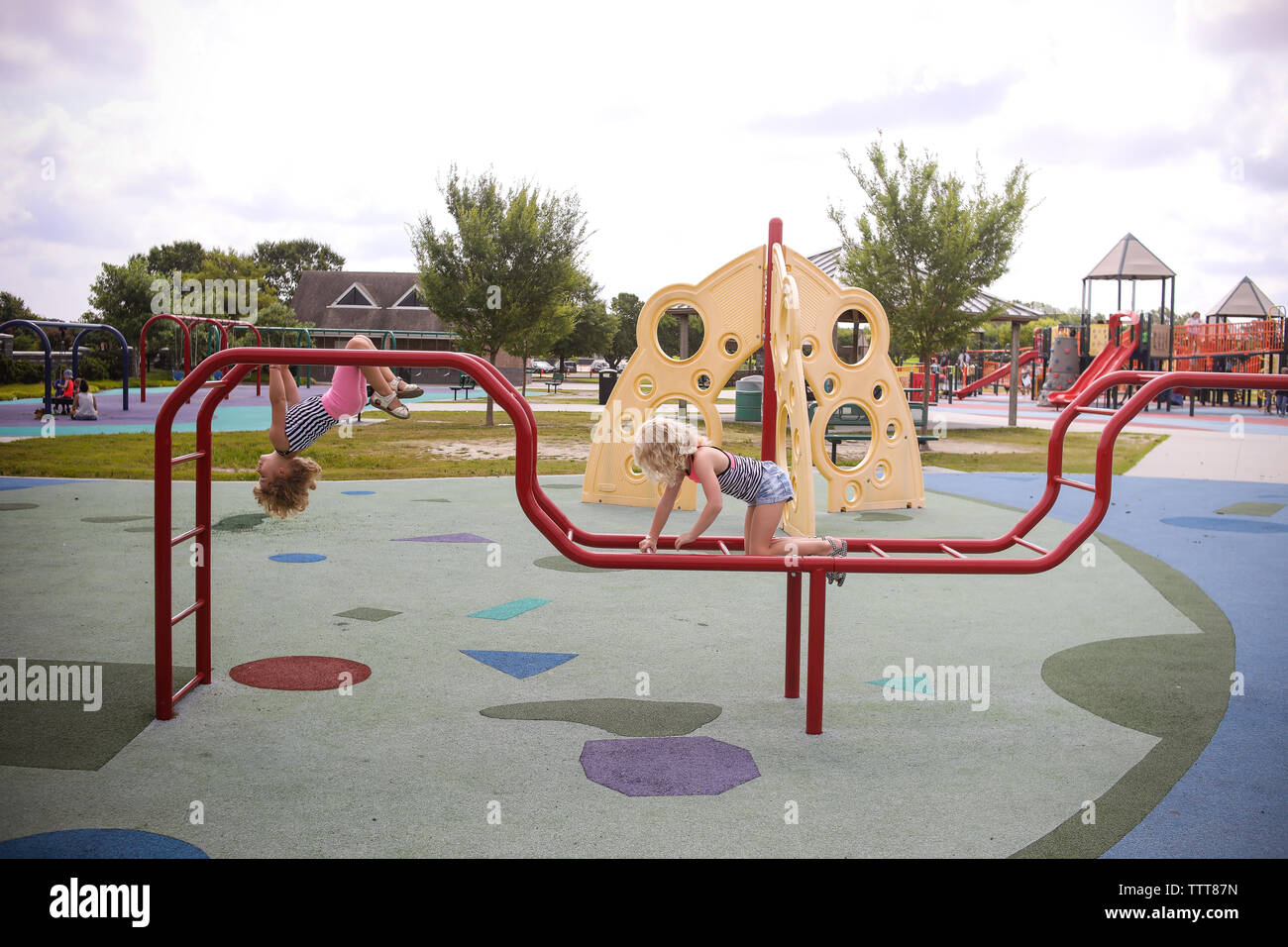 two girls climbing on playground monkey bars upside down Stock Photo