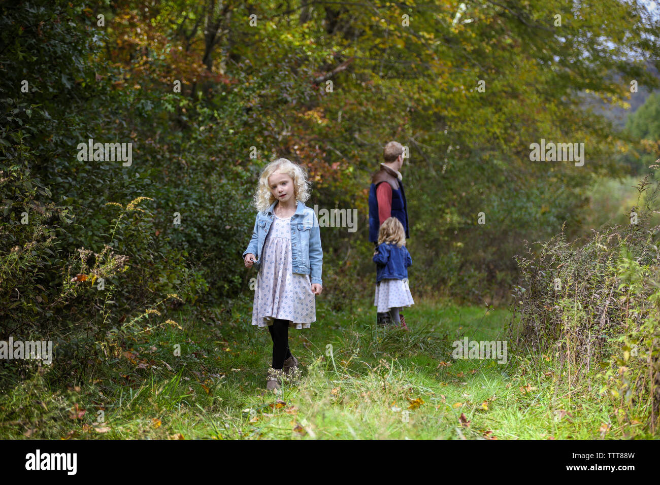 little girl walking away from dad and sister in woods wearing a dress