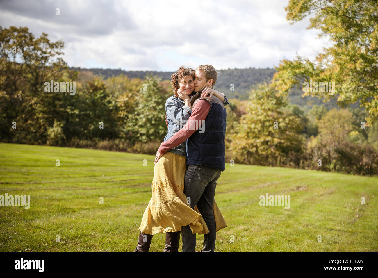 couple embracing together smiling with windblown hair in field Stock Photo