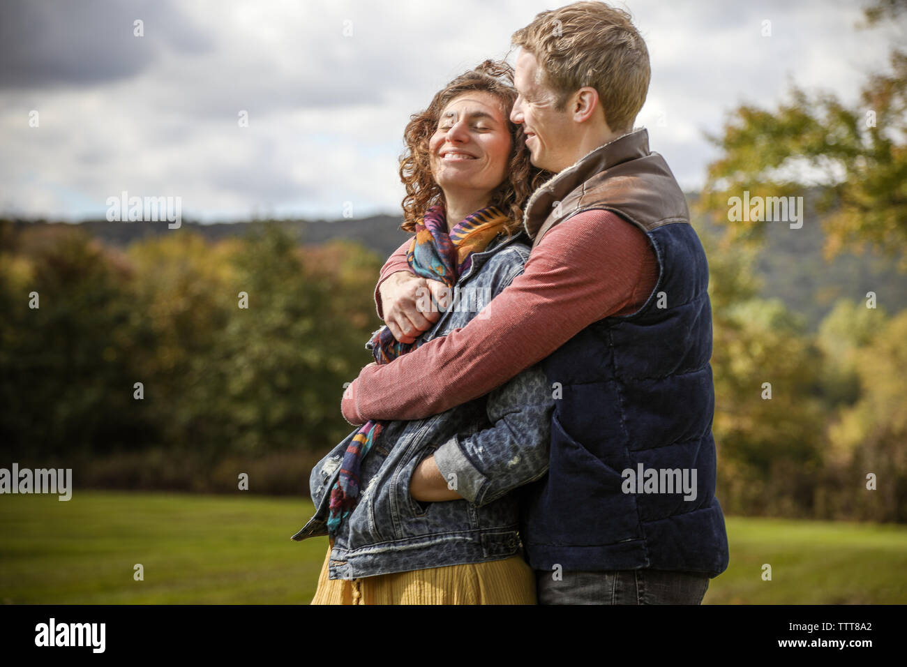 couple embracing in hug smiling and laughing with eyes closed in field Stock Photo