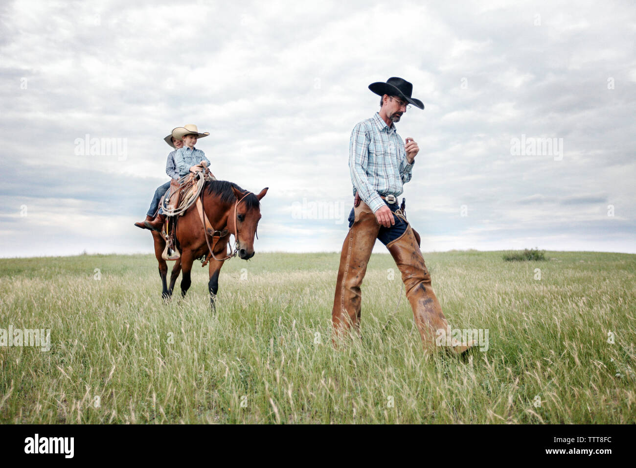 Father walking while sons riding horse on field against cloudy sky Stock Photo