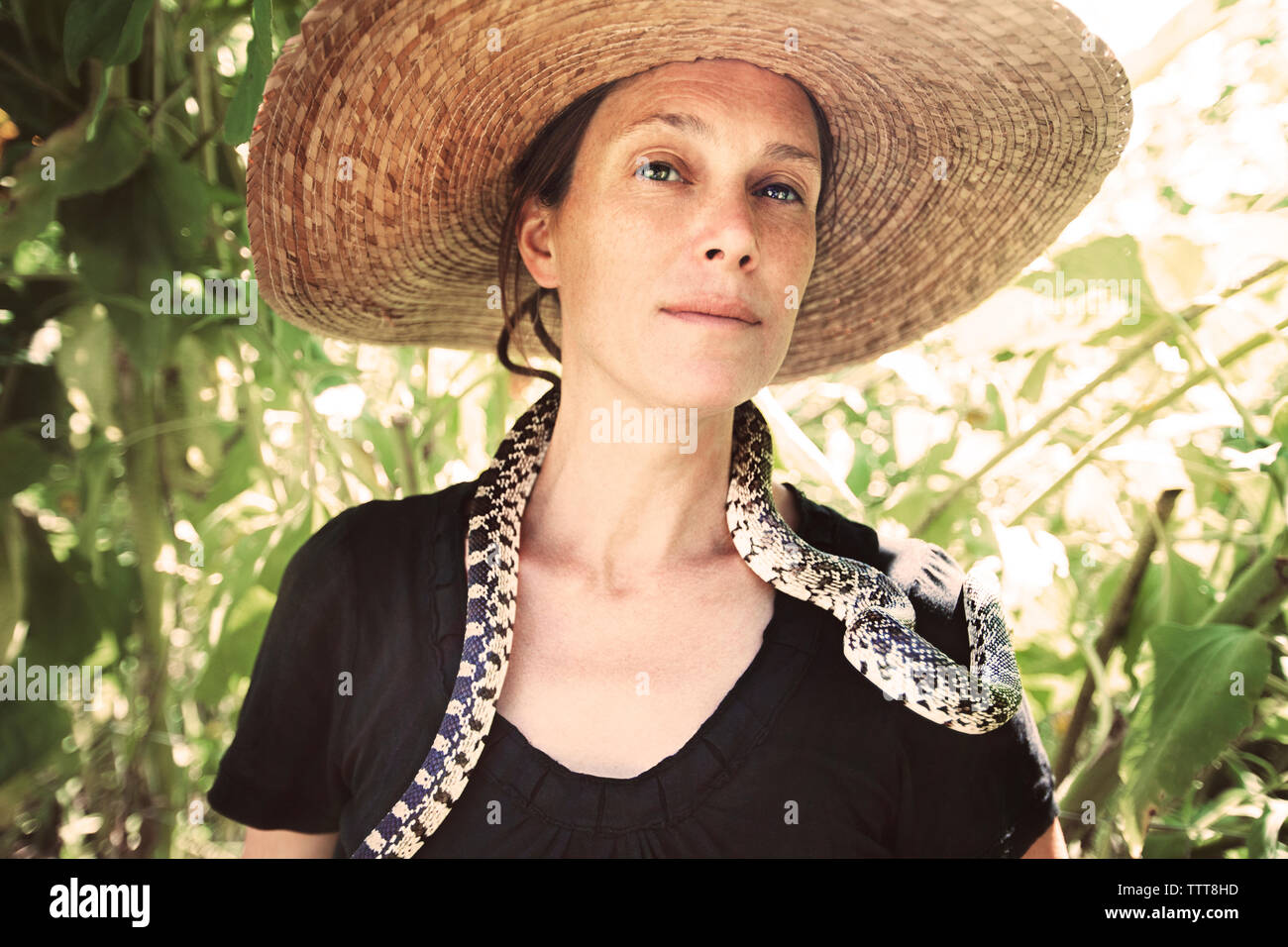 Portrait of confident woman with snake around neck standing in forest Stock Photo