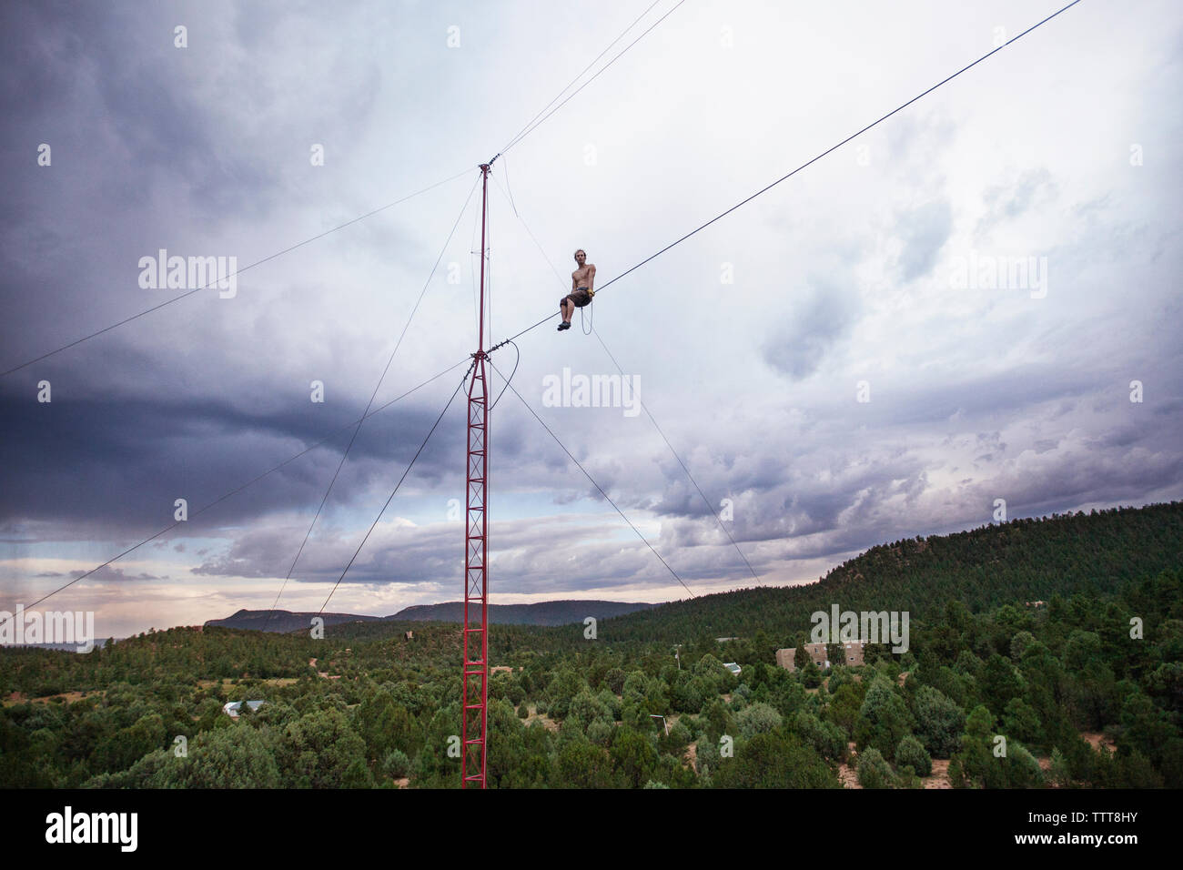 Low angle view of man sitting on tight rope against cloudy sky Stock Photo
