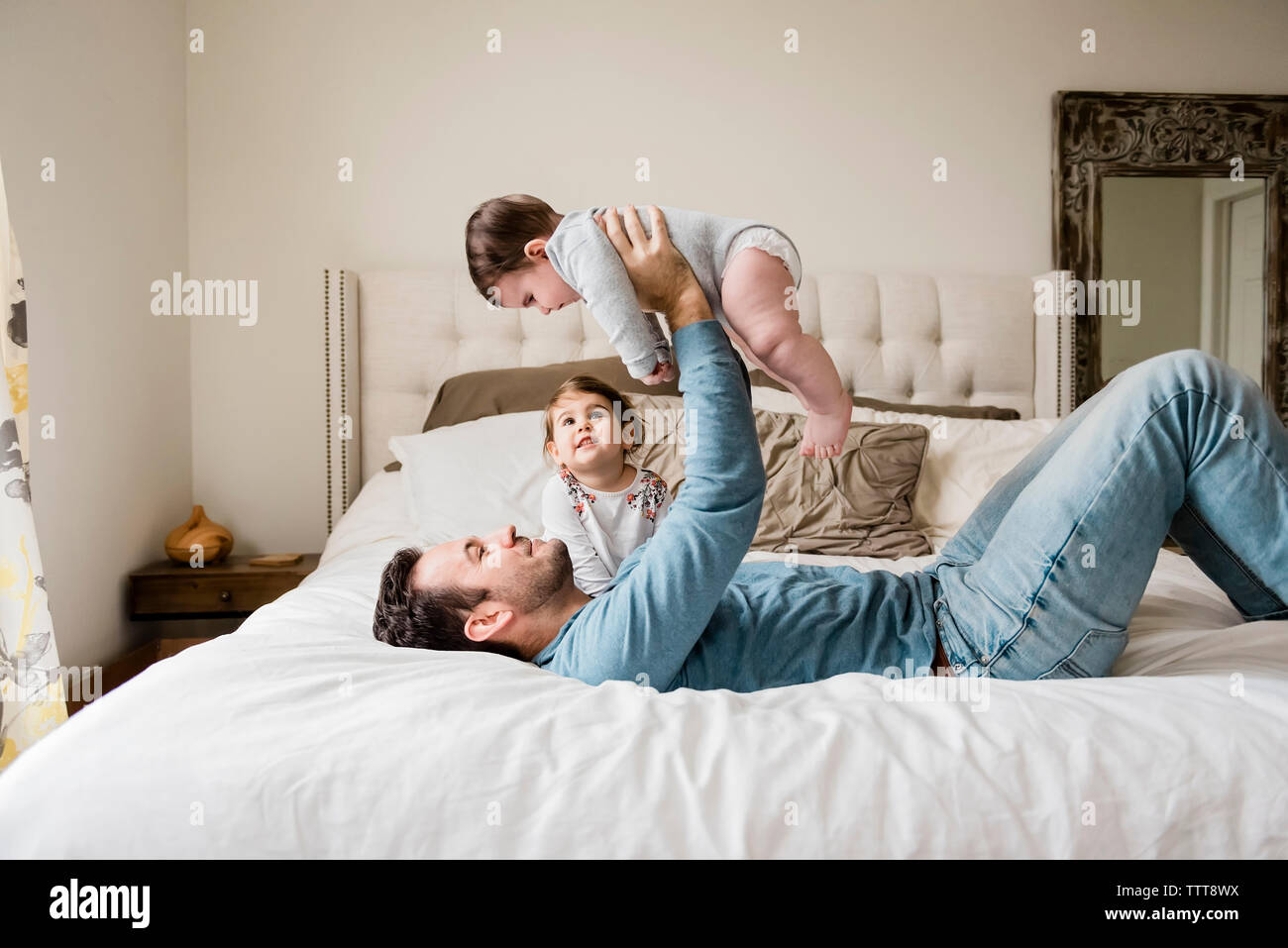 Playful father lifting son while lying by daughter on bed at home Stock Photo